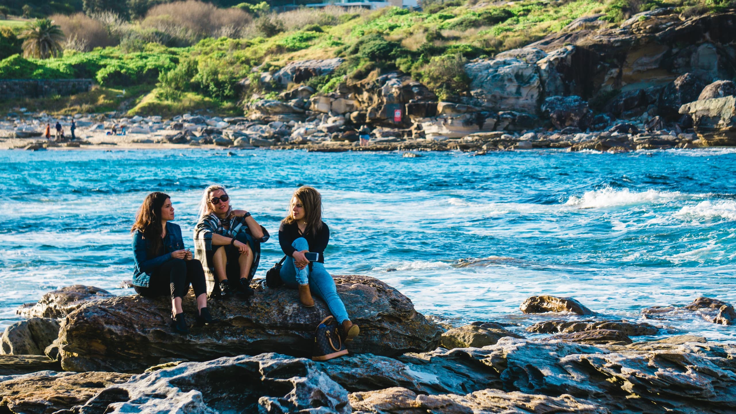 Three women sitting on rocks near river