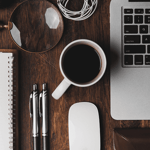 Desk with laptop, coffee mug, pens, mouse, and magnifying glass