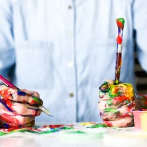 Man holding two paintbrushes with pain on his hands